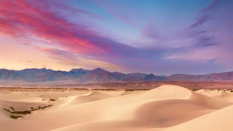 Skies burst with color above the desert and mountain range